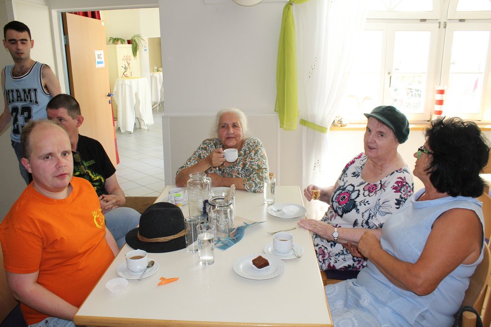 Einige Personen sitzen mit Kaffee und Kuchen zu Tisch.