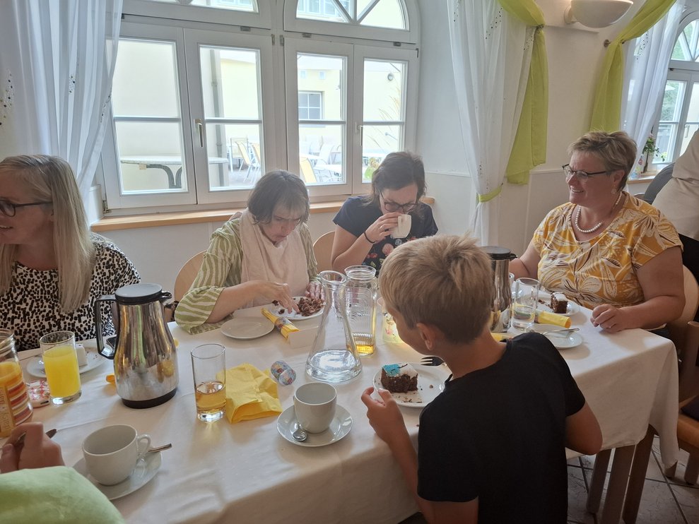 Einige Personen sitzen beim Tisch bei Kaffee und Kuchen