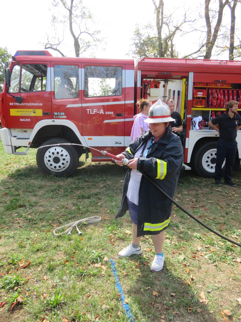 Eine Dame hat eine Wasserschlauch in der Hand und Feuerwehrgewand an.