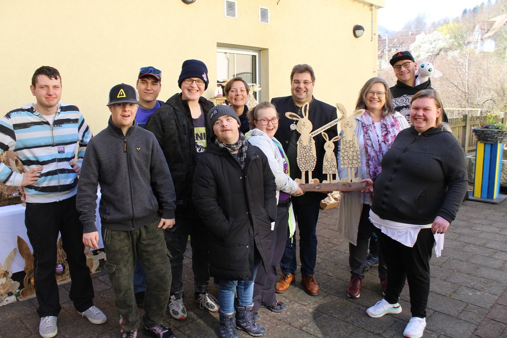 mehrere Personen übergeben zwei Personen drei Osterhasen aus Holz
