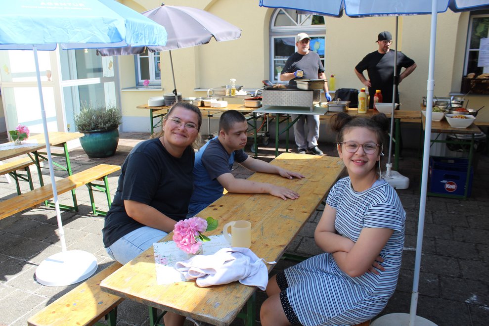 Drei Personen sitzen unter einem Sonnenschirm im Schatten