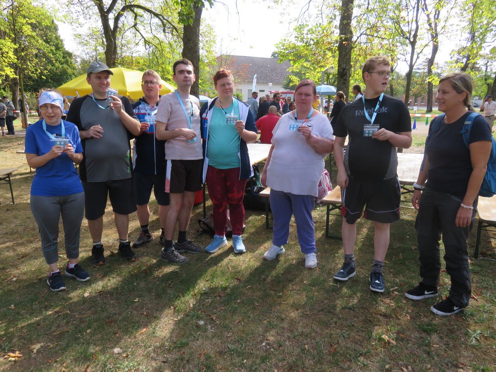 Eine Gruppe Personen steht auf einer Wiese mit Bäumen im Hintergrund.