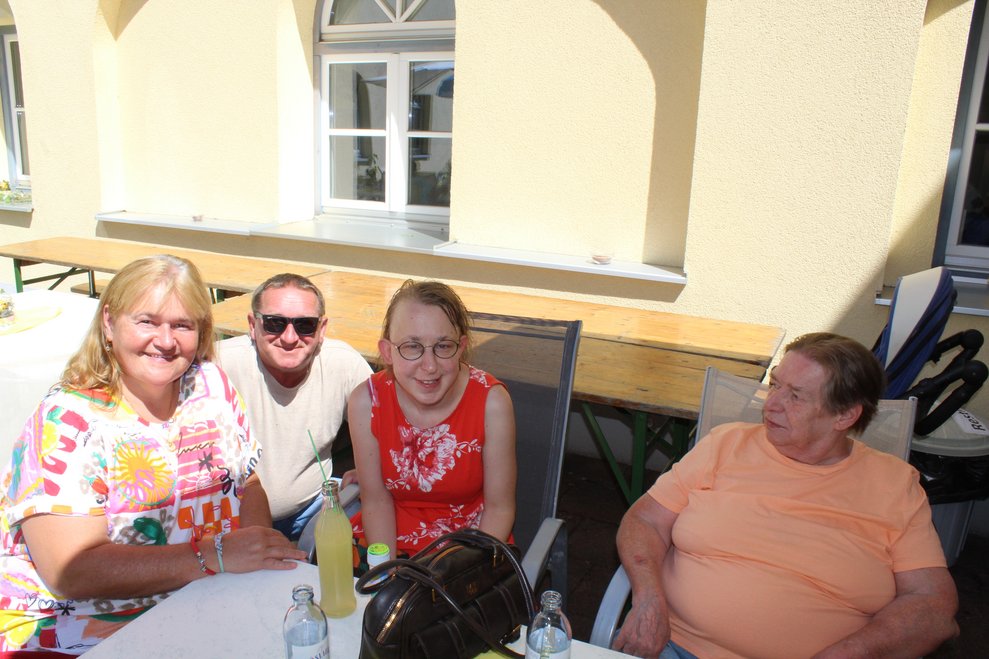 Vier Personen sitzen draußen auf der Terrasse.