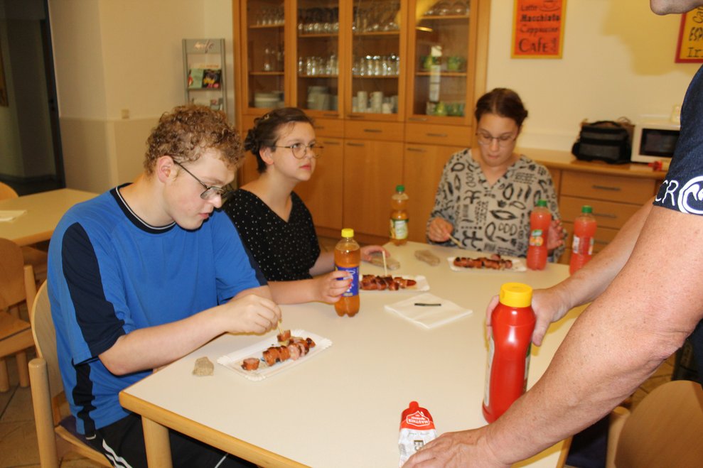 Drei Personen sitzen bei Tisch und essen.