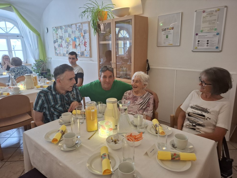Einige Personen sitzen an einem Tisch bei Kaffee und Kuchen