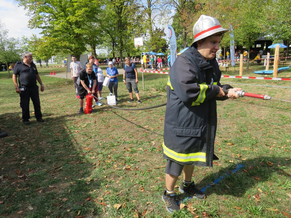 Ein Man hat Feuerwehrgewand an und einen Schlauch in der Hand.