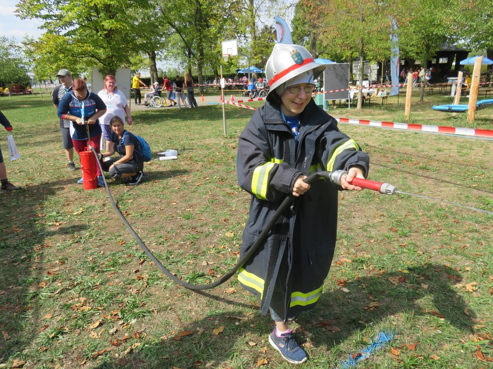 Eine Dame hat Feuerwehrgewand an und einen Schlauch in der Hand.