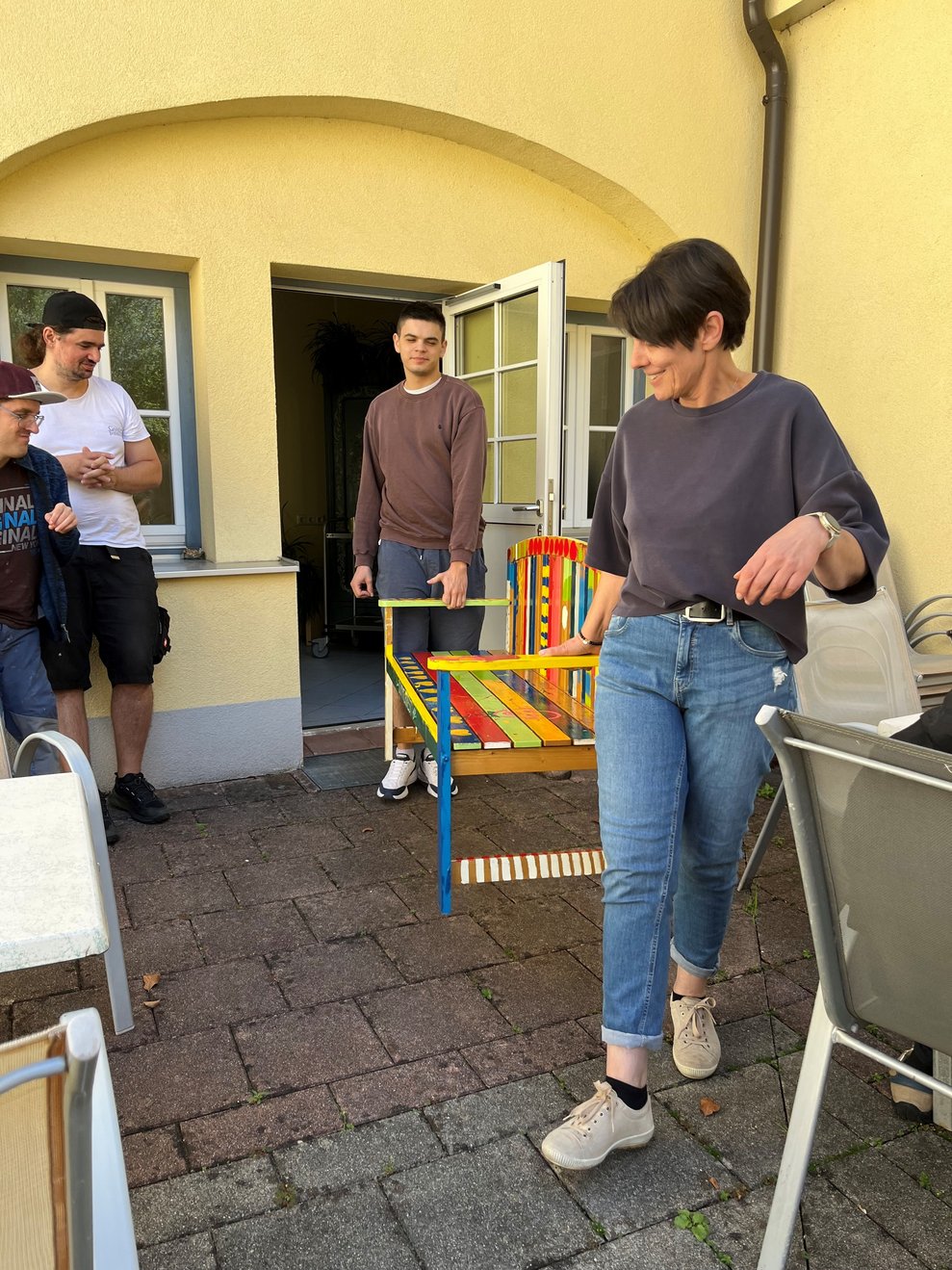 Zwei Personen tragen eine bunte Gartenbank.