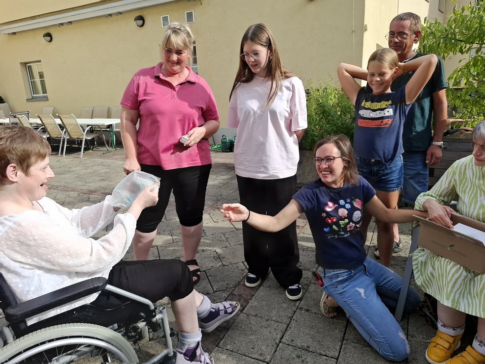 Eine Dame im Rollstuhl steht neben anderen Personen, sie freut sich