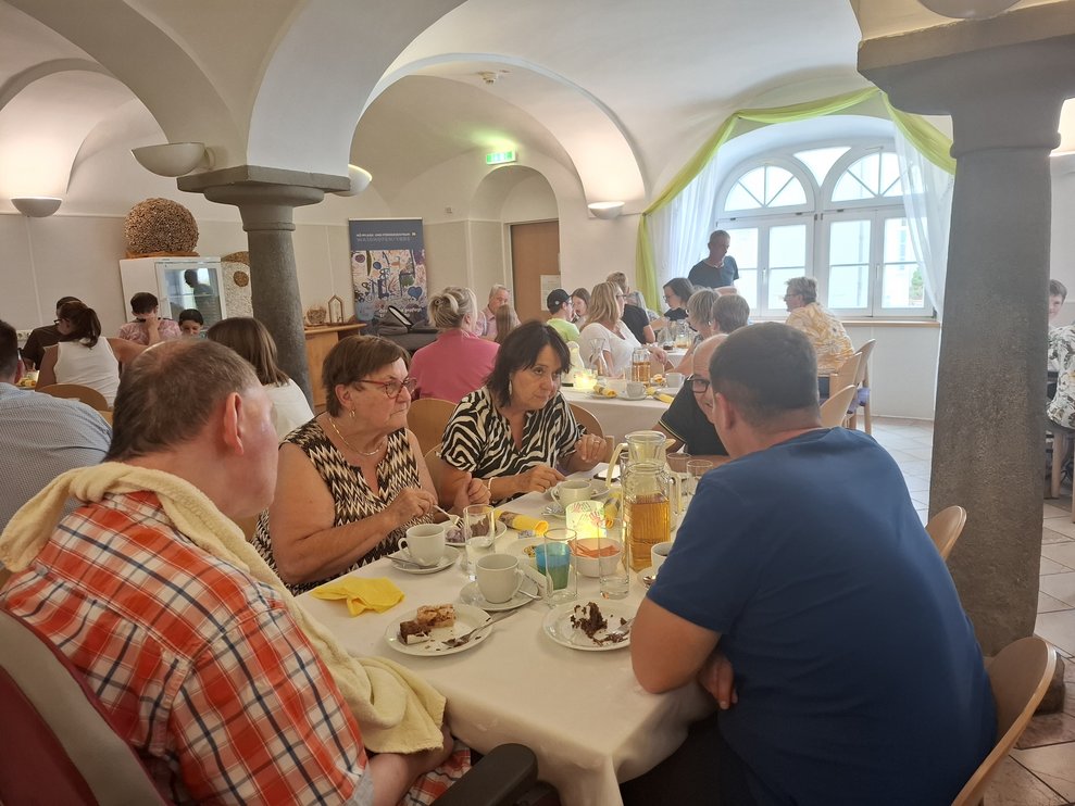 In einem Saal sitzen viele Personen bei Kaffee und Kuchen an Tischen