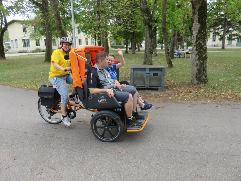 Eine Dame fährt mit einem Rikscha Fahrrad und zwei Personen fahren vorne mit.