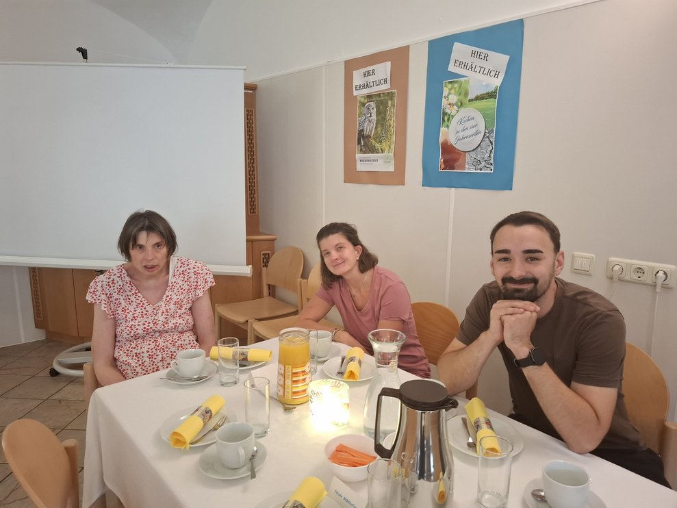 Zwei Damen ein ein Herr sitzen bei einem Tisch