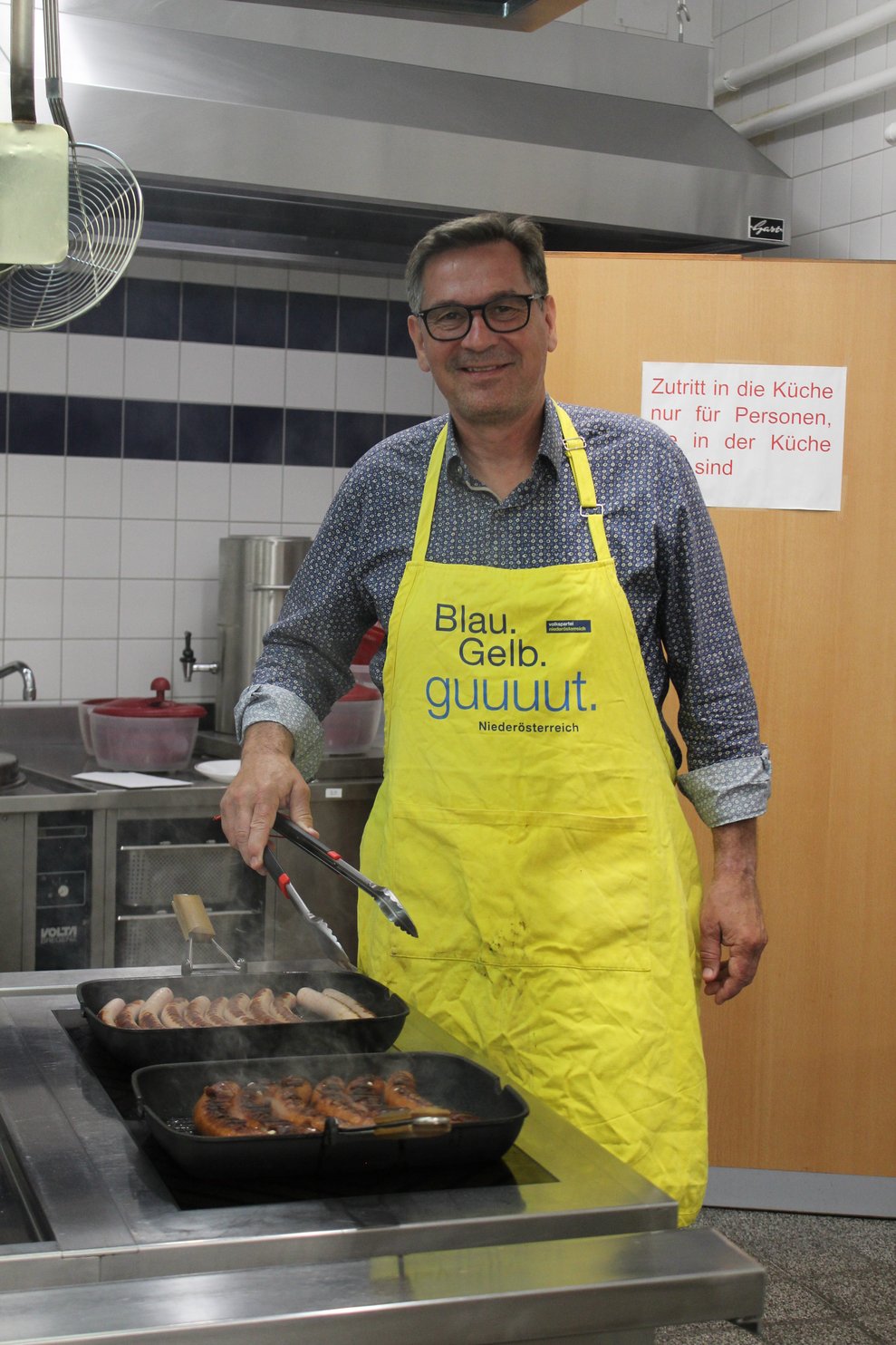 Ein Mann bereitet Grillwürstel in einer Pfanne zu