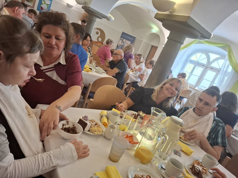 Mehrere Personen sitzen zu Tisch bei Kaffee und Kuchen